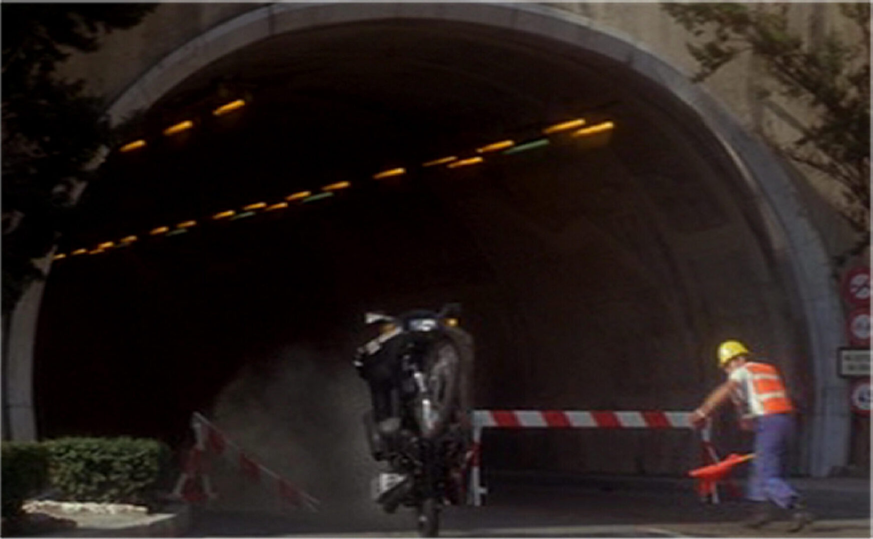 Bond on Q-Branch motor bike, wheelies and smashes through a barrier.